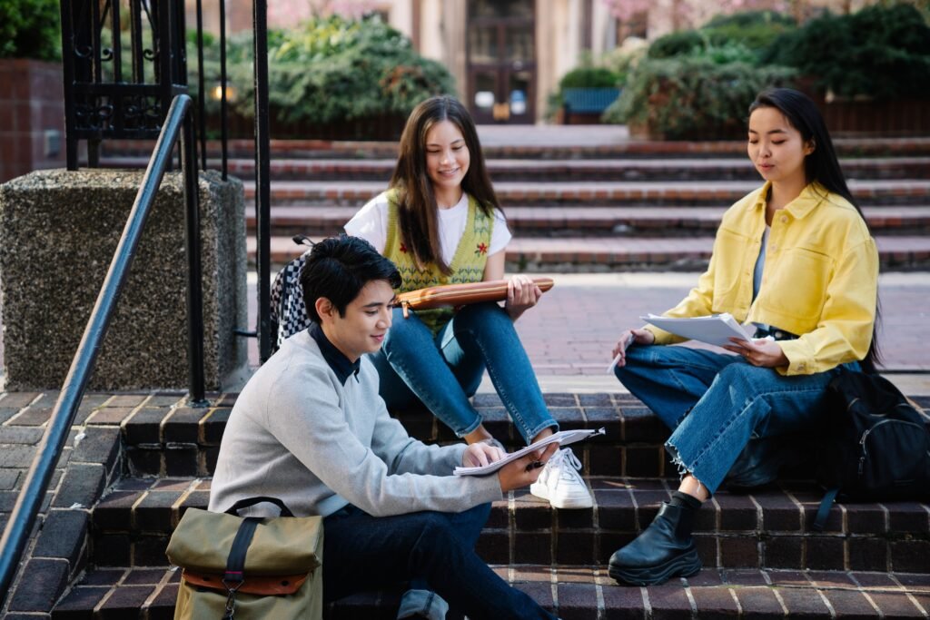 Group of students studying outdoors on college campus steps, enjoying sunny day.